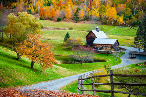 Eine ländliche Szene in Kanada mit einem Bauernhaus, einem kleinen Teich und sanften Hügeln, umgeben von bunten Herbstwäldern